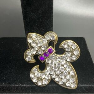 fleur-de-lis brooch or pendant decorated with clear and purple rhinestones.